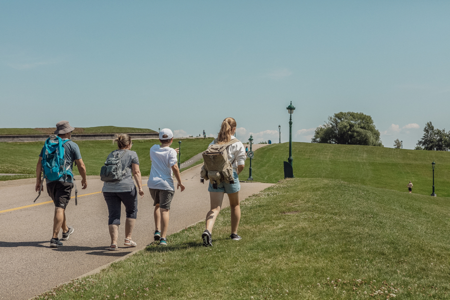 Four people walking along a path in the Plains of Abraham park on a sunny day.