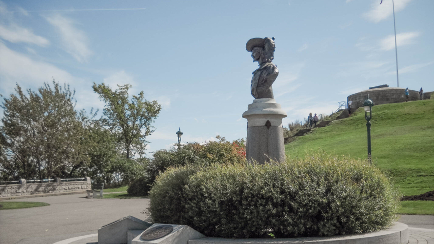 Image du monument Pierre-Dugua-de-Mons situé sur la terrasse Pierre-Dugua-de-Mons, sur le territoire des plaines d'Abraham. Le monument commémore l'importance de la culture française au Canada. Pierre Dugua de Mons est une figure clé de la colonisation de la Nouvelle-France. La statue est placée sur un fond de paysage magnifique des plaines d'Abraham. // Image of the Pierre-Dugua-de-Mons monument located on the Pierre-Dugua-de-Mons Terrace, within the Plains of Abraham. The monument commemorates the importance of French culture in Canada. Pierre Dugua de Mons is a key figure in the colonization of New France. The statue is set against the beautiful landscape of the Plains of Abraham.