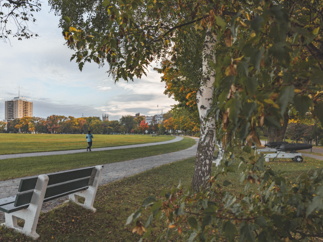 Park bench with a person jogging on an autumn day, with cannons visible in the background. Banc de parc avec une personne faisant du jogging un jour d'automne, des canons visibles en arrière-plan.