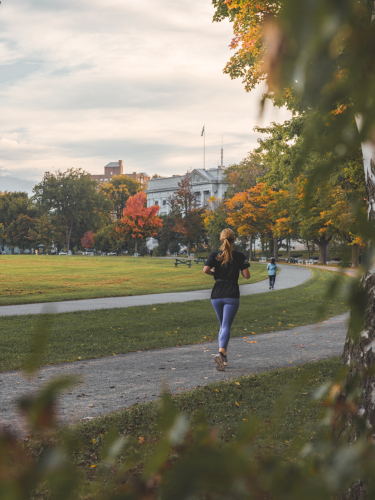 Two people jogging on a track in autumn, surrounded by trees with colorful leaves. Deux personnes faisant du jogging sur une piste en automne, entourées d'arbres aux feuilles colorées.
